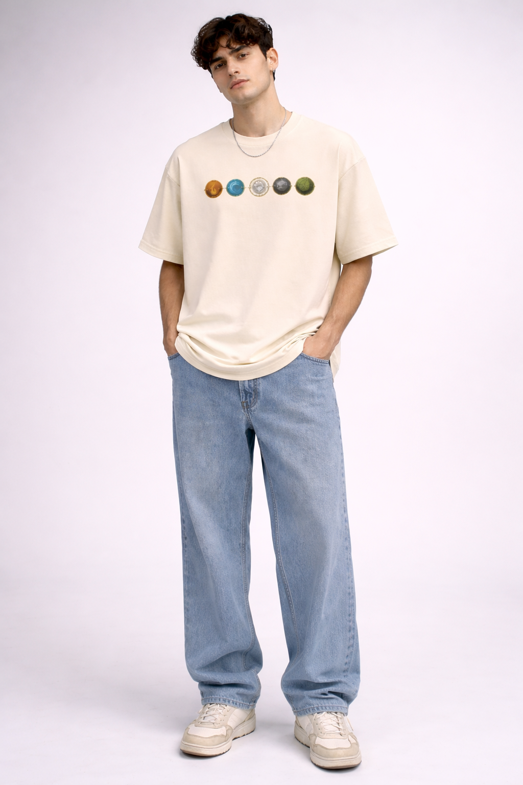 Person wearing a beige t-shirt with planet graphics and light blue jeans on a white background