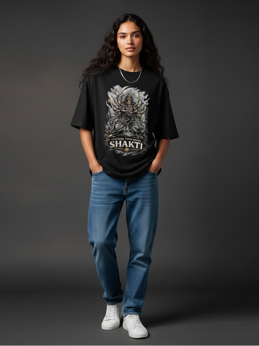 Person wearing a Durga inspired black t-shirt with 'Shakti' design and blue jeans on a dark background. exclusive durga puja and kali puja design