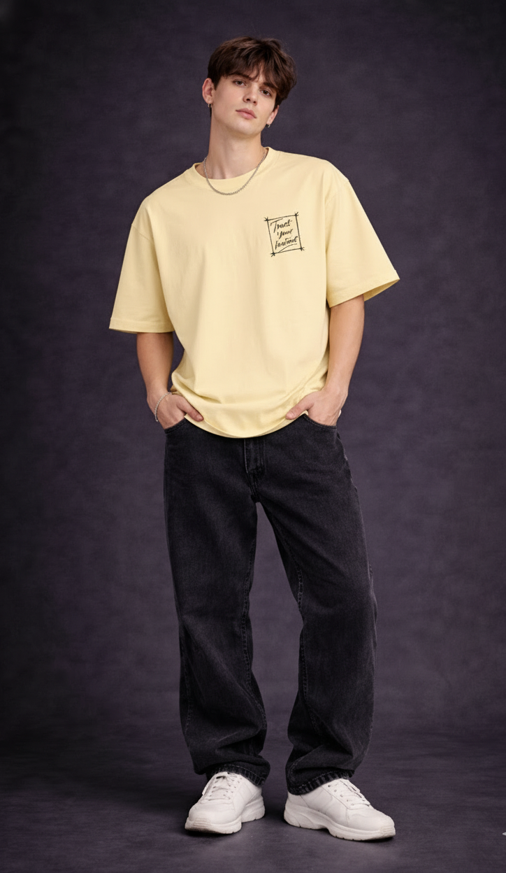Model wearing an oversized pale yellow crewneck t-shirt with a small chest graphic, paired with black jeans.