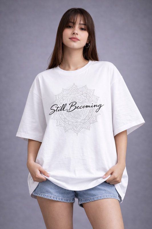 Model in an oversized white cotton graphic tee with a circular mandala print and script text, paired with casual jean shorts.